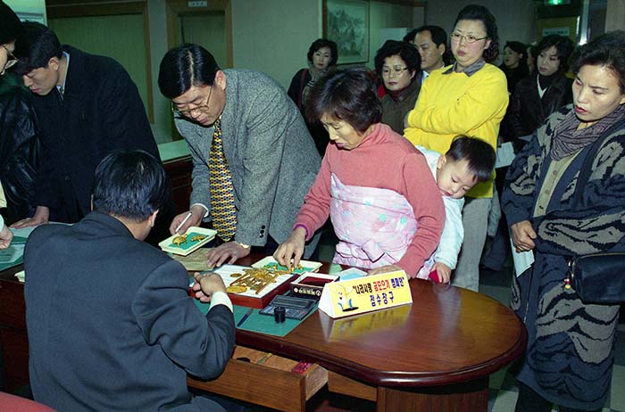 한국은 1997년 금융위기를 극복하기 위해 국제통화기금(IMF)에 지원을 요청했고, 경제회복을 위해 국민 모두가 노력을 기울였다. 특히 금모으기 운동에 동참하기 위해 아이를 업고 돌반지를 가져온 엄마(사진)를 비롯해 길게 줄을 선 사람들의 모습에서 국민의 단결력을 확인할 수 있다.